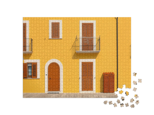 Puzzle 1000 pezzi „Una pittoresca facciata gialla con porte, balconi e finestre marroni nel centro storico di Termoli“