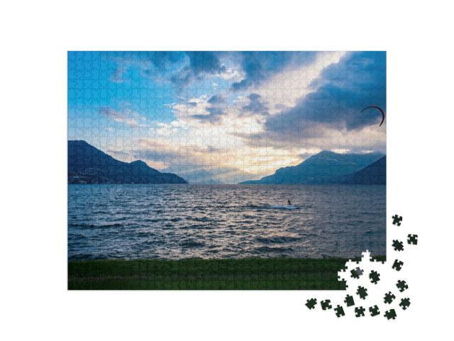 Puzzle 1000 pezzi „Panorama del Lago di Como, a Dervio, con barche a vela e i raggi del sole che illuminano il lago.“