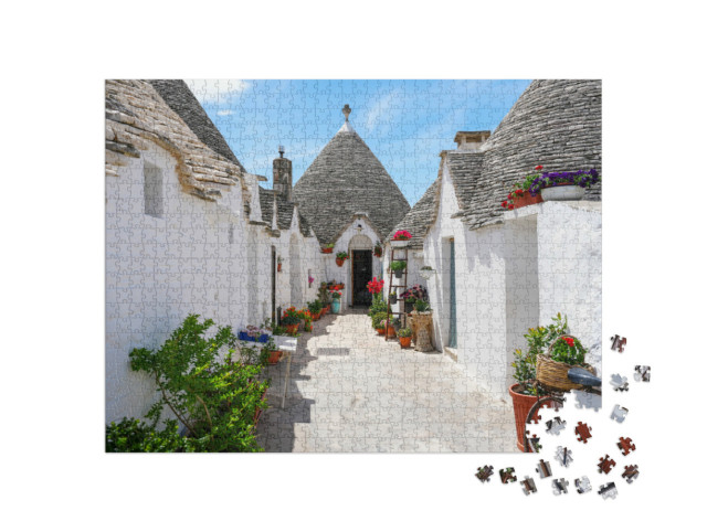Puzzle 1000 pezzi „Fiori colorati di fronte alla tradizionale casa a trulli di Alberobello“